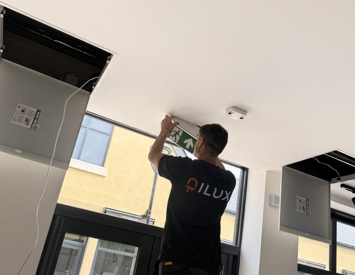 An ILUX engineer fitting an emergency exit sign above a shop entrance