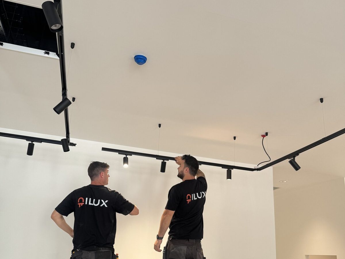 Two ILUX engineers installing track lighting in a new retail unit