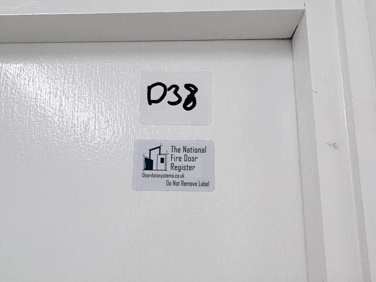 A fire door register asset label on the top edge of a fire door