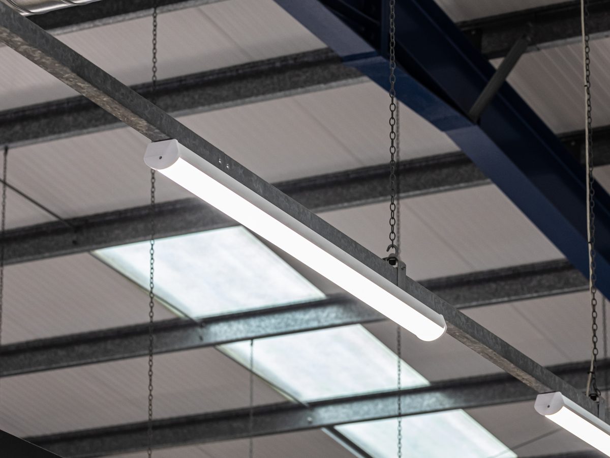 Close-up of a new white LED batten suspended on chains from the galvanised lighting trunking below a store roof